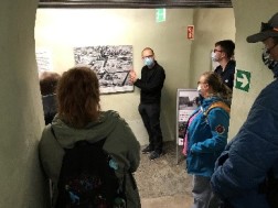 Referent steht bei einer Ausstellungsführung vor einem historischen Plan des Geländes während ihm Besucher*innen zuhören