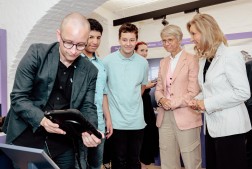 Es sind fünf Personen zu erkennen. Vorne links hält eine Person ein Tablet in der Hand. Die vier anderen Personen blicken auf das Tablet.